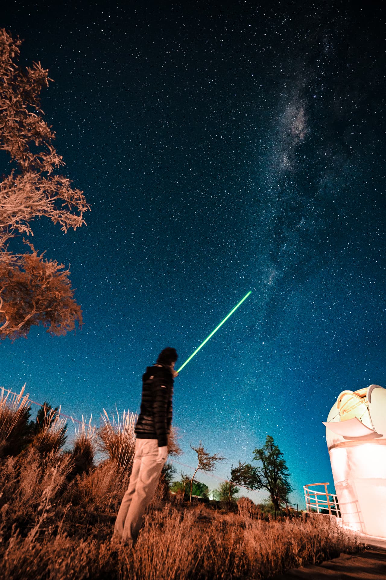 A retreat participant pointing a laser at the Milky Way beside an observatory dome in the Atacama Desert