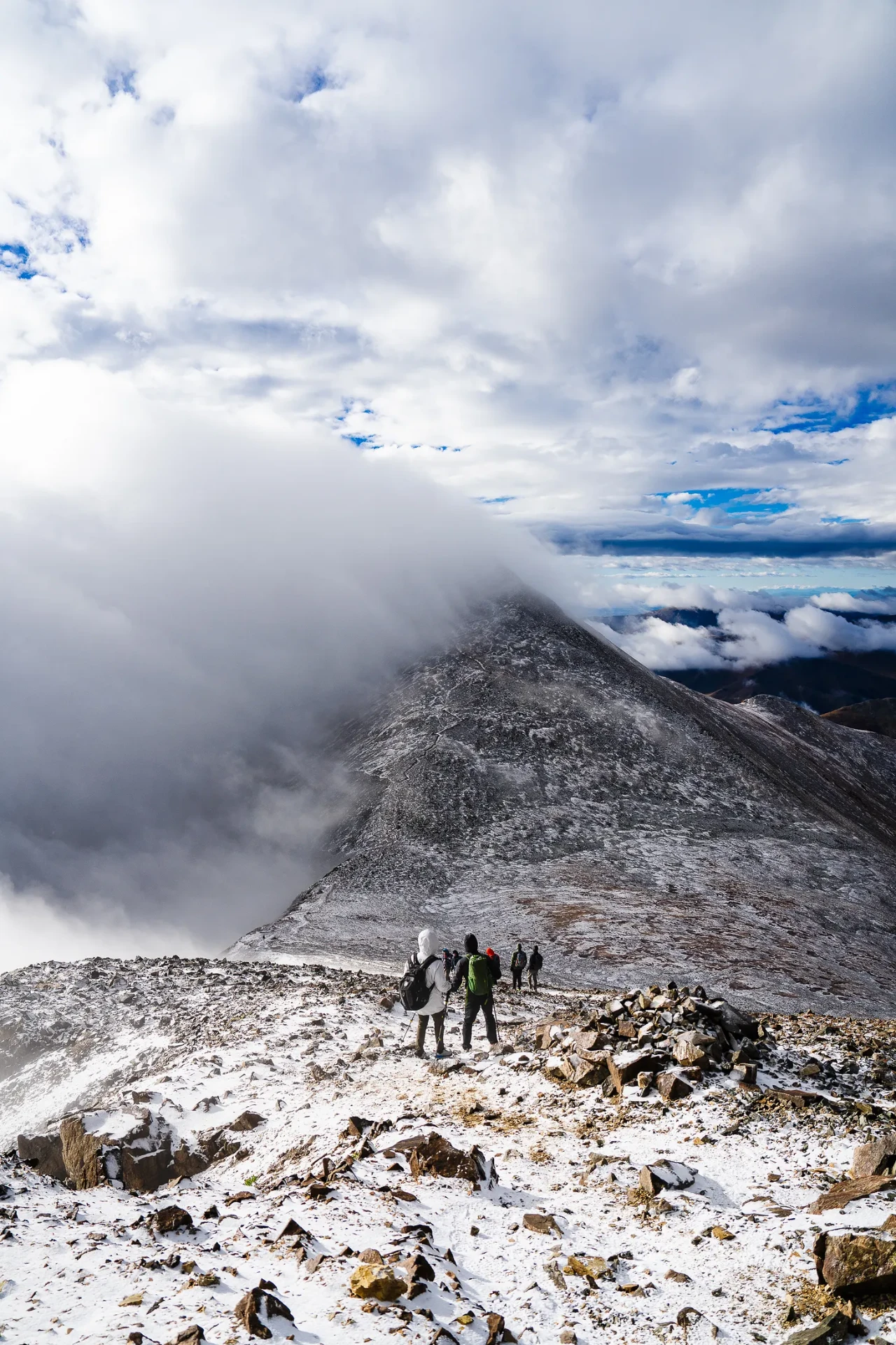 Climbers pausing below a snow-dusted summit shrouded in drifting cloud