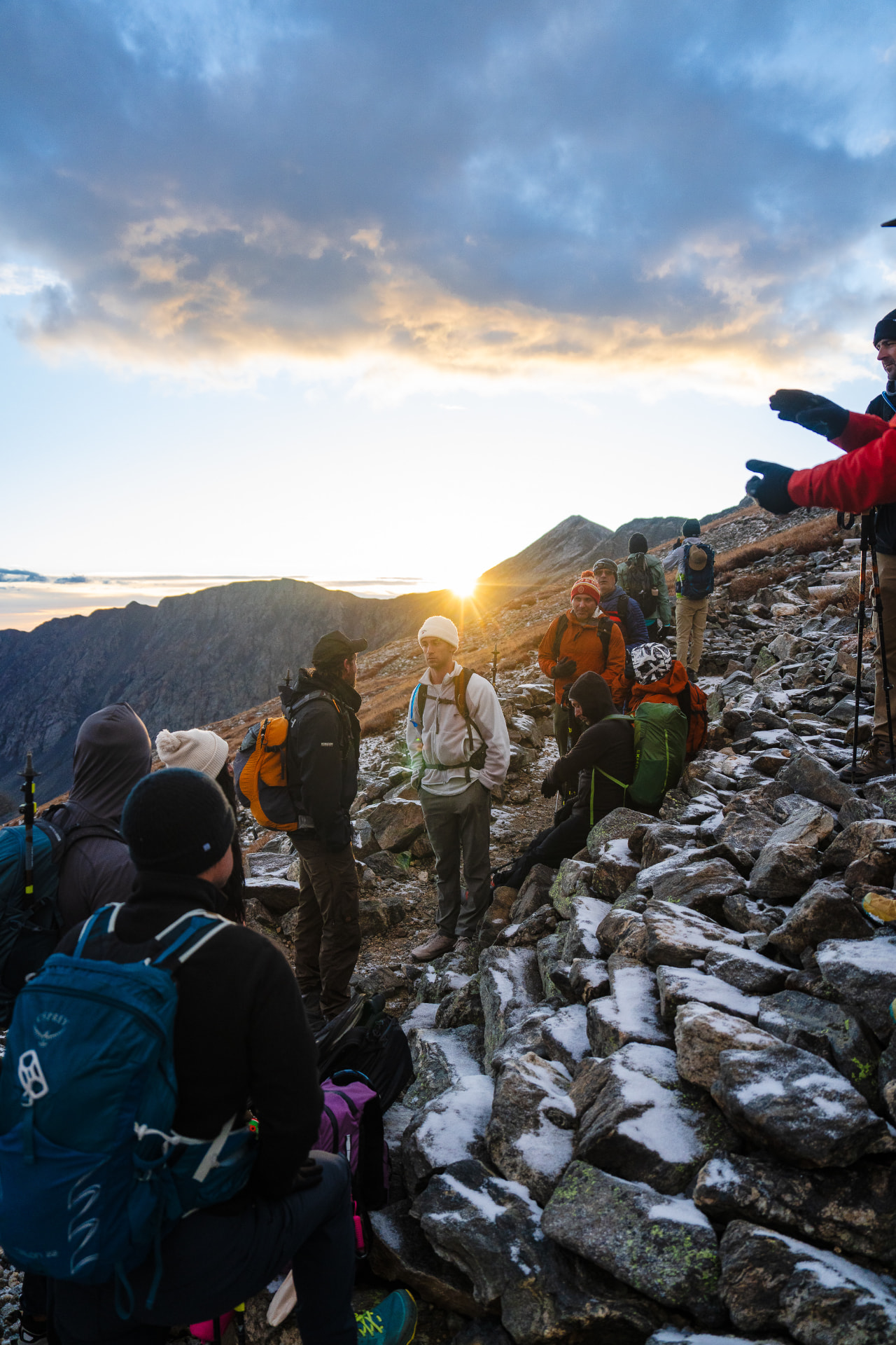 The team pausing on a rocky ridge at dawn as the sun breaks over the peaks
