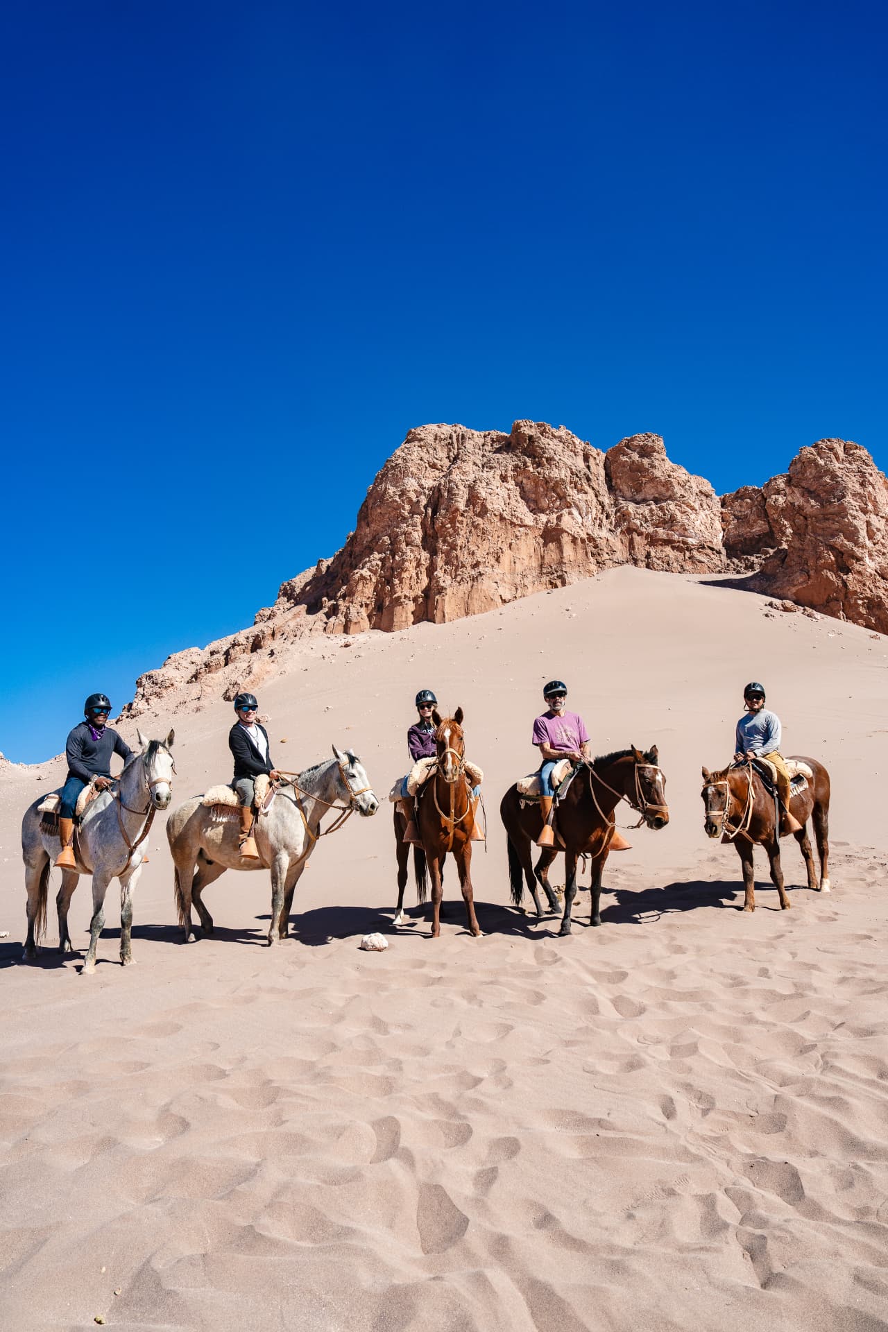 Five riders on horseback lined up in a red sand canyon under a deep blue sky