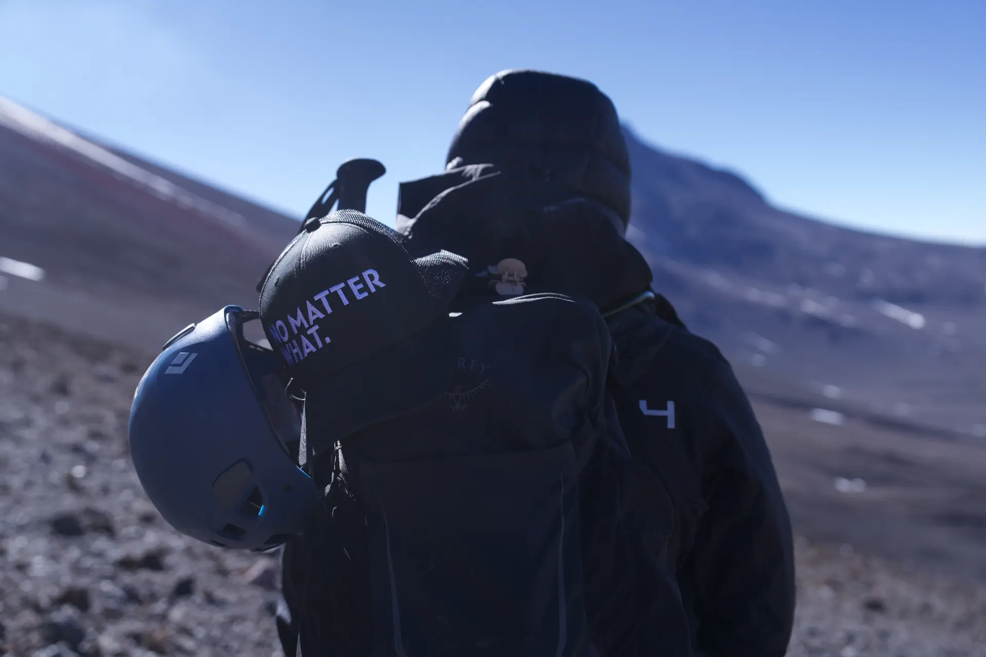 A No Matter What participant on a high mountain route, cap clipped to their pack